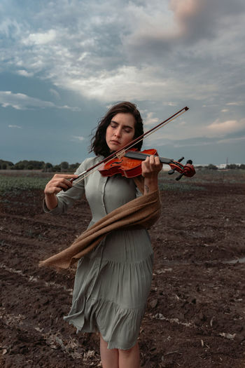 WOMAN HOLDING UMBRELLA STANDING ON FIELD AGAINST SKY