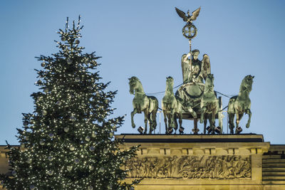 Low angle view of christmas tree and statue against clear sky at dusk