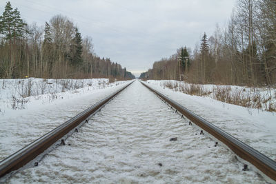 Railroad tracks by snow covered trees against sky