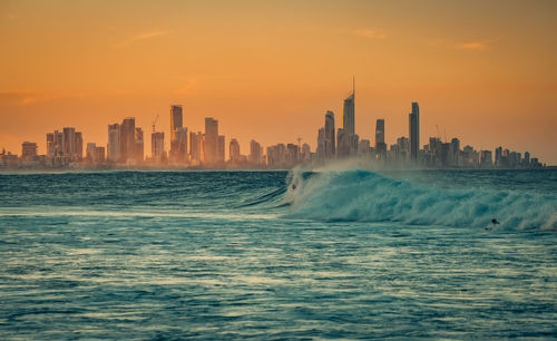 Sea by buildings against sky during sunset