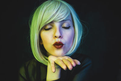 Close-up of mid adult woman with blond hair blowing kiss against black background