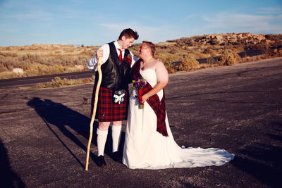 Full length of lesbian couple smiling at each other while wearing wedding dress