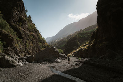 Woman walking at rocky mountains against sky