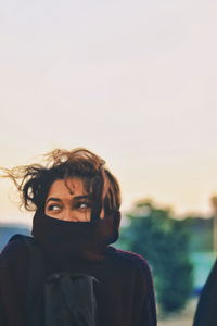 Woman in warm clothing looking away during sunset