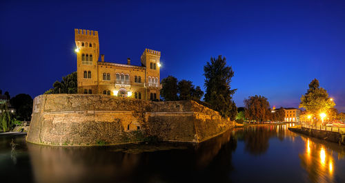 Illuminated building by lake against sky at night