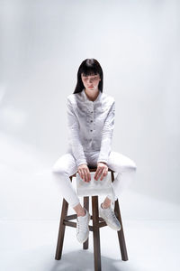 Portrait of young woman with arms crossed standing against white background