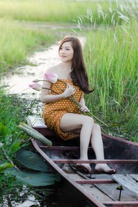 Young woman with flowers looking away while sitting on old boat against plants