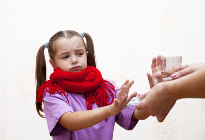 Daughter refusing medicine and drinking water by mother against white background