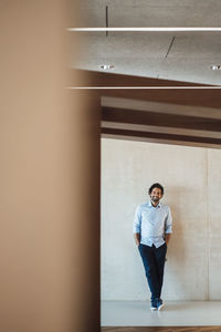 Smiling businessman with hands in pockets at corridor