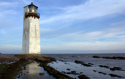 Lighthouse by sea against sky