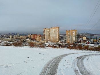 Snow covered road by buildings in city against sky