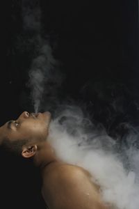 Side view man exhaling smoke over black background