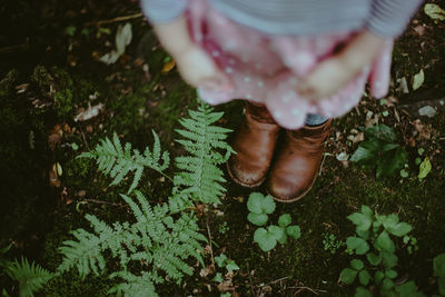 Low section of girls boots standing on ground near plants