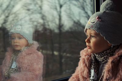 Cute girl looking through window while sitting at home during winter