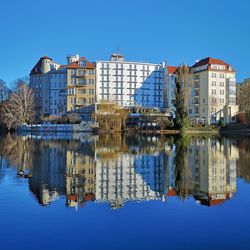 Reflection of buildings in lake against clear blue sky