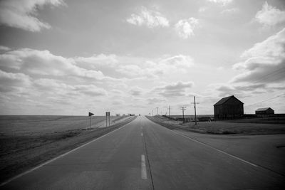 Empty road amidst field against cloudy sky