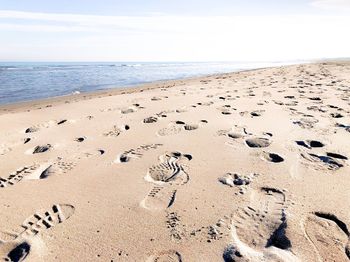 Footprints on sand at beach against sky