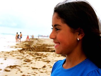 Side view of smiling girl at beach against sky