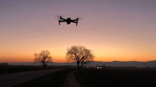 Low angle view of silhouette drone flying against sky during sunset