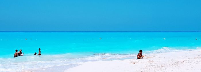 People on beach against clear blue sky