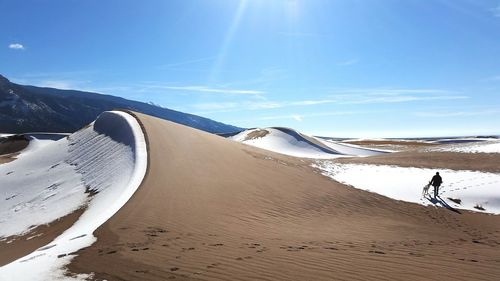 Woman with dog walking on snow covered land against blue sky