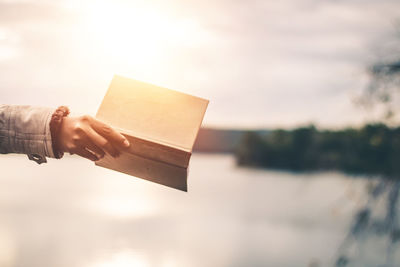 Midsection of person holding paper against sky