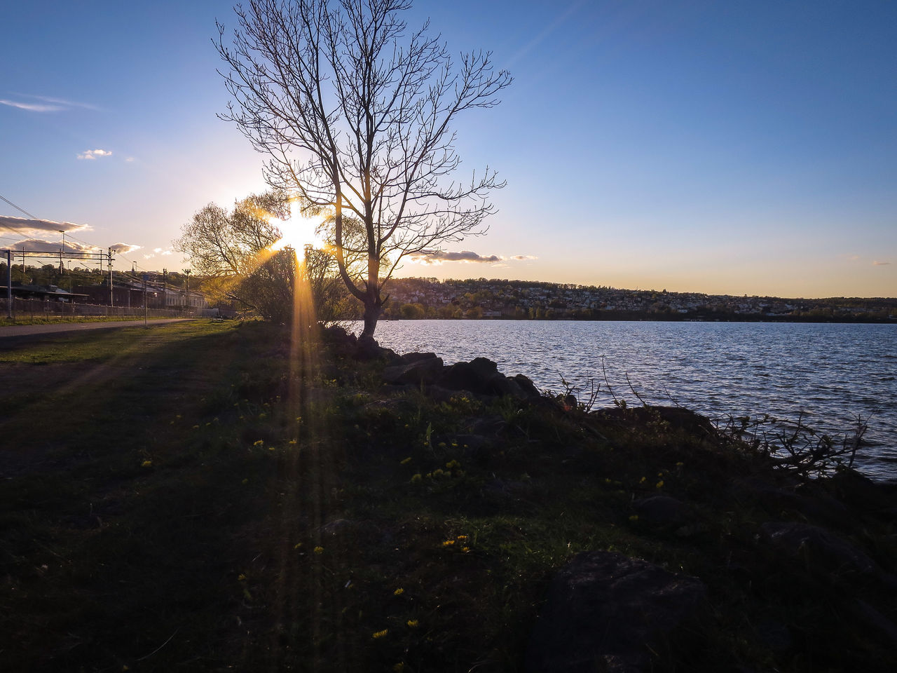 sunset, tranquil scene, sun, tranquility, water, scenics, beauty in nature, sunlight, nature, silhouette, sky, lake, tree, idyllic, landscape, clear sky, sunbeam, blue, lens flare, sea