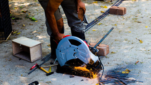 Low section of man cutting metal on field 