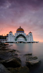 Building by sea against sky during sunset