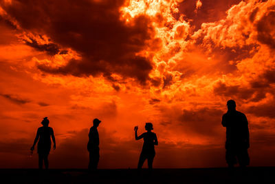 Silhouette people standing against orange sky