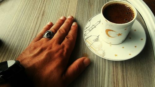 Close-up of hand holding coffee cup on table