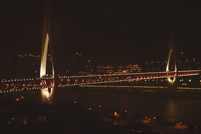 Illuminated bridge over river against sky at night