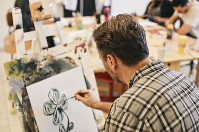 Mature male student practicing painting on artist's canvas in art class