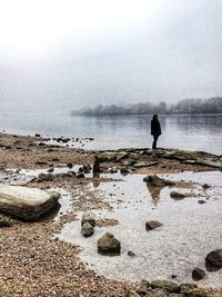 Man standing on rock by sea against sky