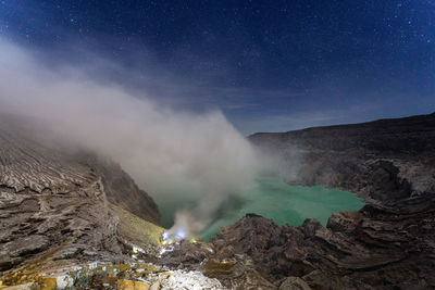 Smoke emitting from volcanic mountain against sky at night