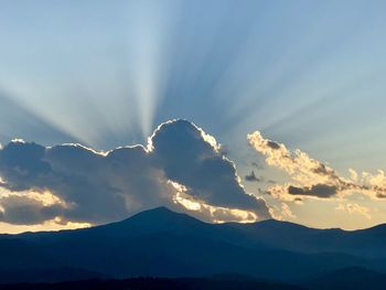 Sunlight streaming through silhouette mountain against sky