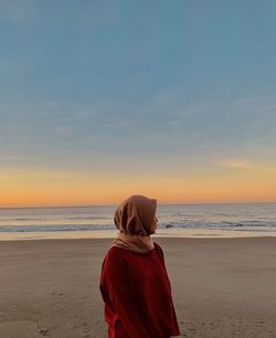 Rear view of woman looking at sea against sky during sunset