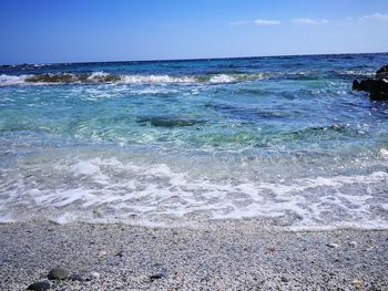 Close-up of waves splashing on beach against blue sky