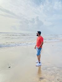 Rear view of man standing at beach against sky