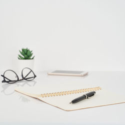 Close-up of book with pen and mobile phone on table against white background