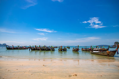 Boats moored on beach against blue sky