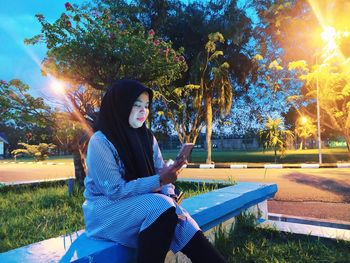 Portrait of young woman sitting on bench at park