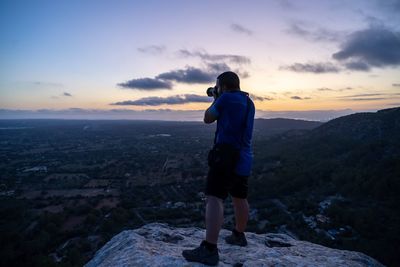Rear view of man photographing against sky during sunset