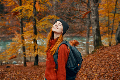 Smiling young woman standing in forest during autumn