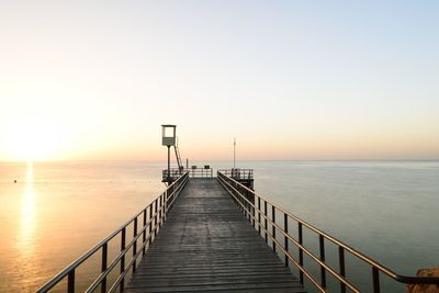 Jetty leading to calm sea at sunset