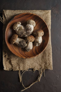 Porcini mushroom on wooden bowl on brown background.