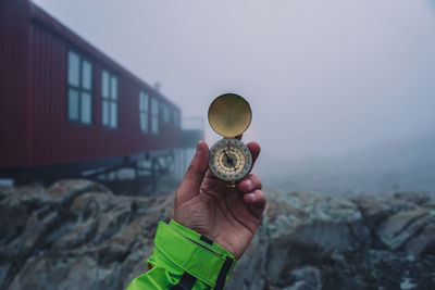 Close-up of hand holding navigational compass against sky