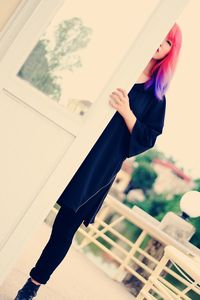 Low angle view of young woman with dyed hair standing by door against clear sky