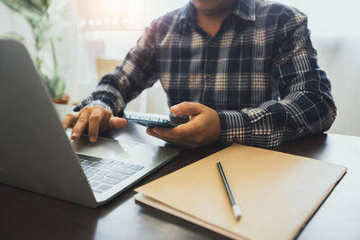 Midsection of man using mobile phone while sitting on table