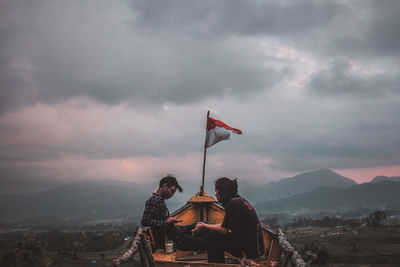 People looking at flag on mountain against sky